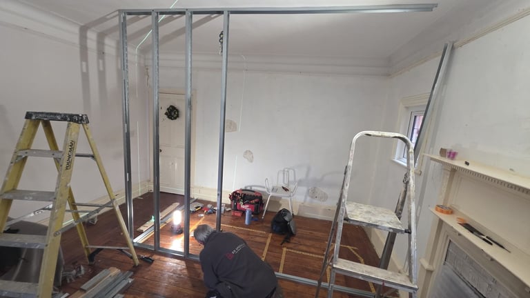 Interior room under renovation with metal framing structure, ladders, and construction materials on wooden floor