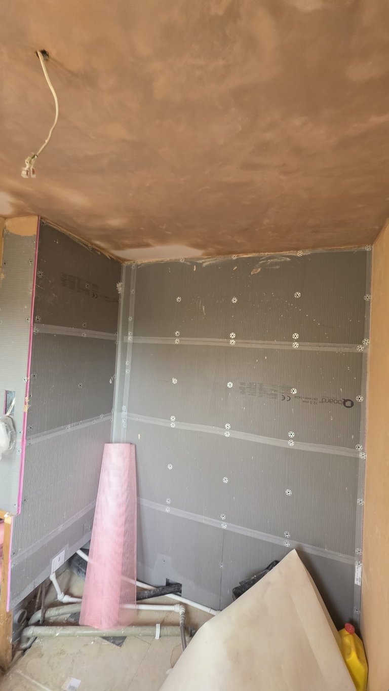 Unfinished drywall shower enclosure under construction with metal framing, primer coating, and construction materials inside