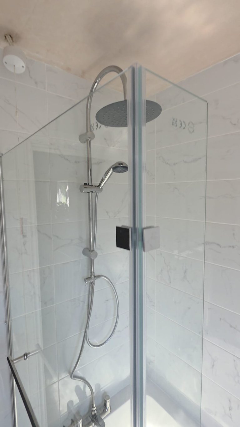Modern glass shower enclosure with rainfall showerhead, handheld sprayer, and metal fixtures in a marble-tiled bathroom