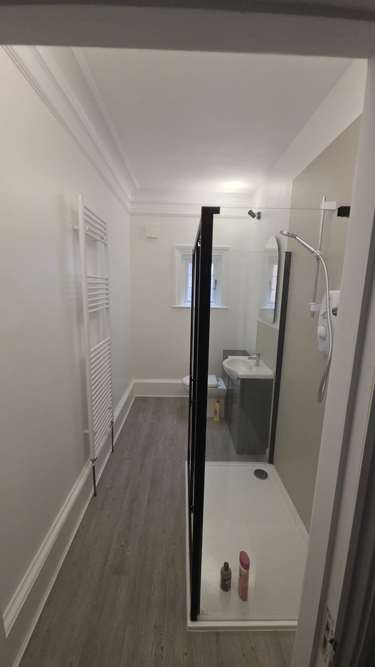 Modern bathroom with walk-in shower enclosure, white walls, wood-look flooring, white cabinetry, and towel rack on left wall.