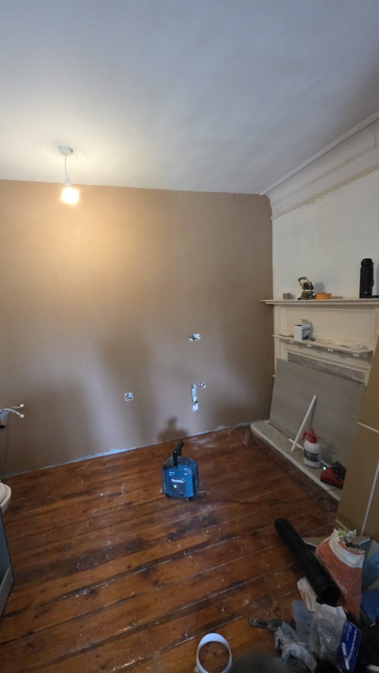Room under renovation with bare walls, wooden flooring, ceiling light, and shelving units along the right side