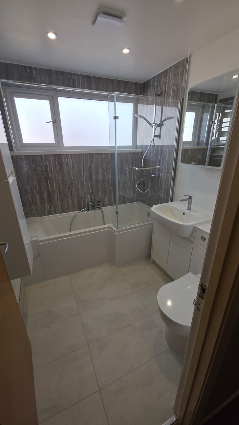 Modern bathroom with dark wood tiled walls, glass shower enclosure, white toilet, sink with vanity, and bright ceiling lights