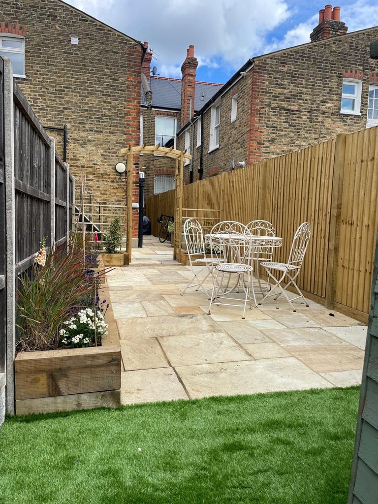 Brick townhouses with a back garden patio featuring white metal furniture, artificial grass, and wooden fence
