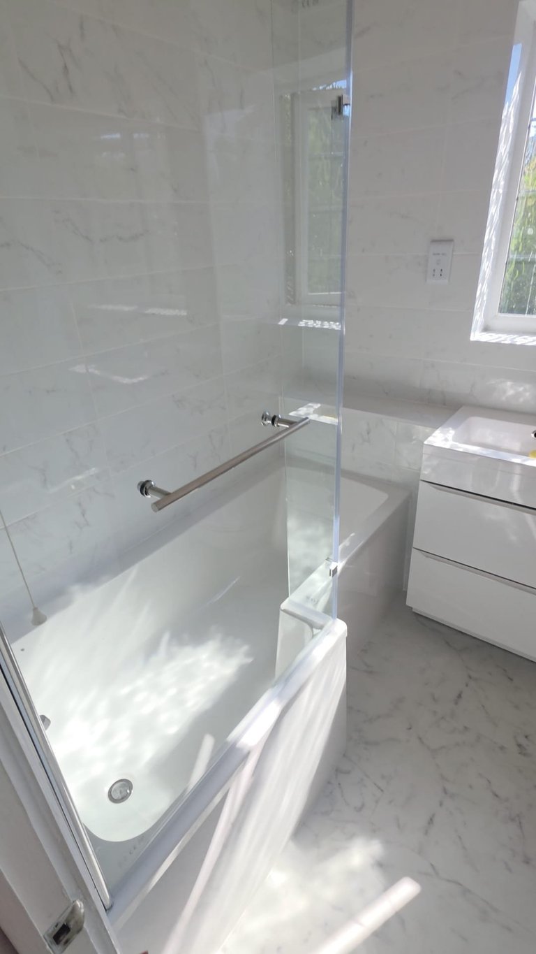 Modern white marble bathroom with glass shower enclosure and white bathtub, bright natural lighting from window