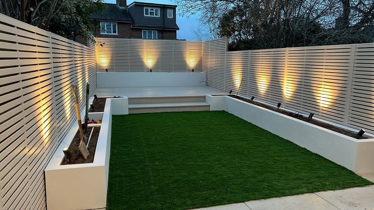 Modern backyard with artificial green lawn, horizontal slatted fences, illuminated uplighting, and white planters