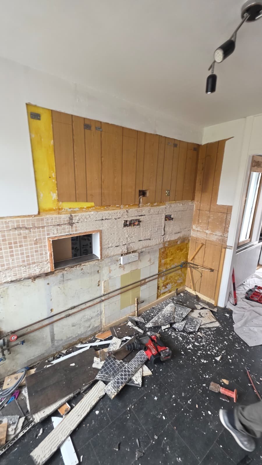 Kitchen renovation in progress with yellow cabinetry, exposed walls, debris scattered on floor, and deteriorated backsplash