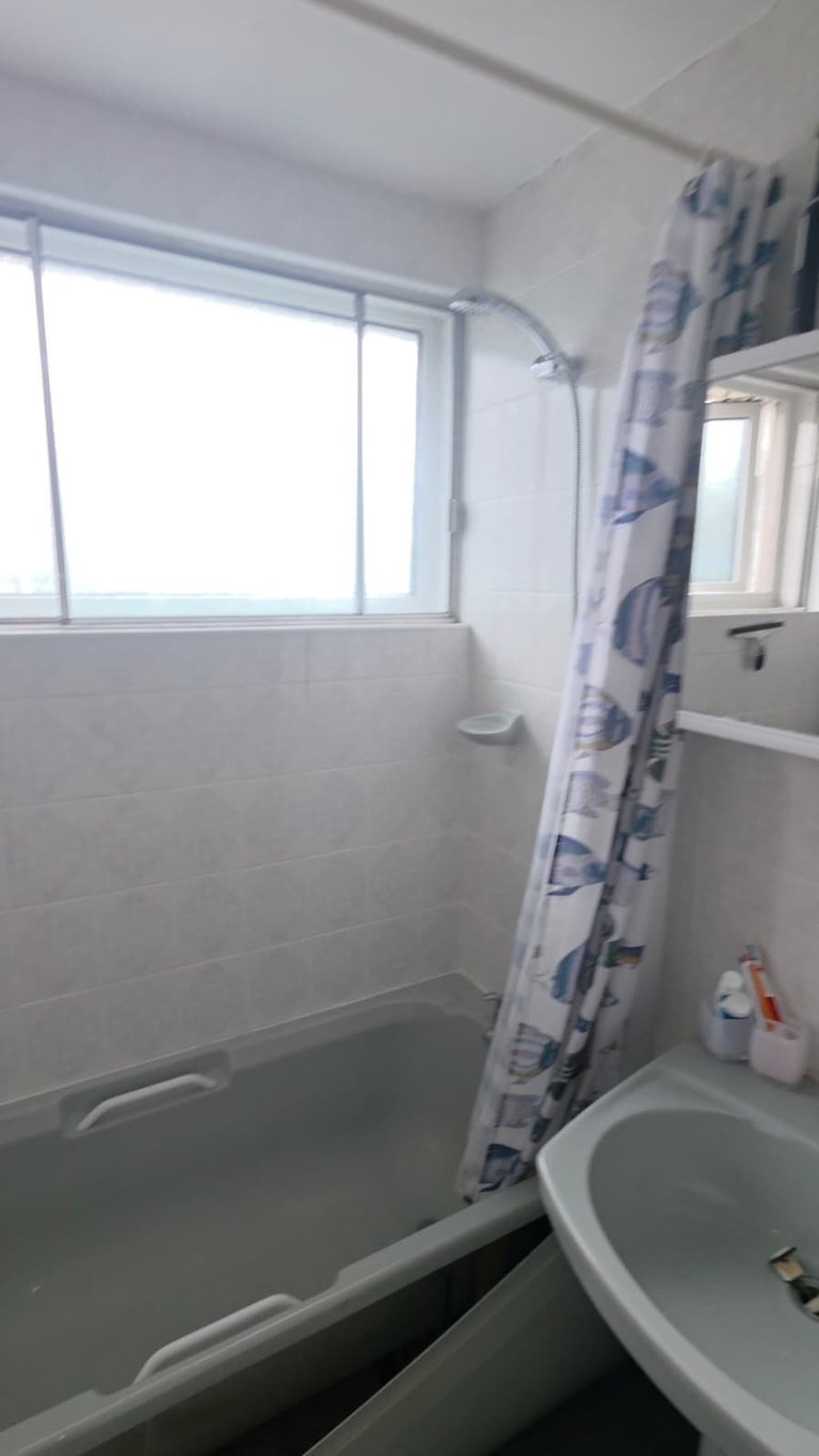 Small bathroom with white tile walls, bathtub with blue patterned shower curtain, round sink, and window with natural light
