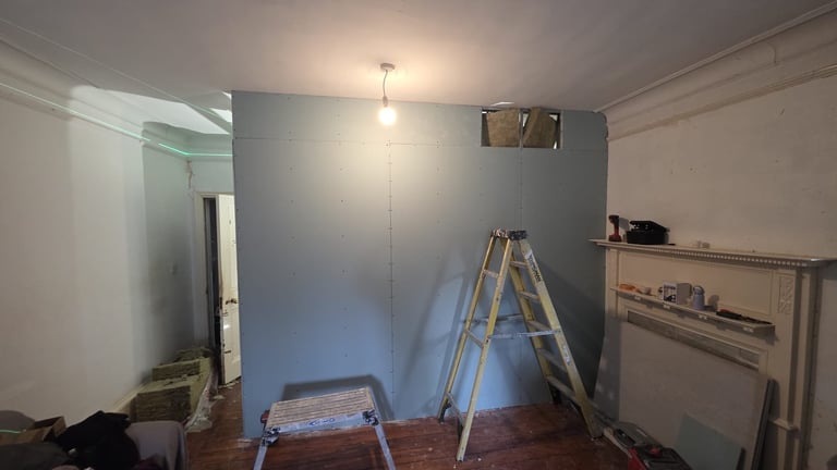 Interior room under renovation with wooden ladder, work bench, exposed walls, and pendant light fixture hanging from ceiling