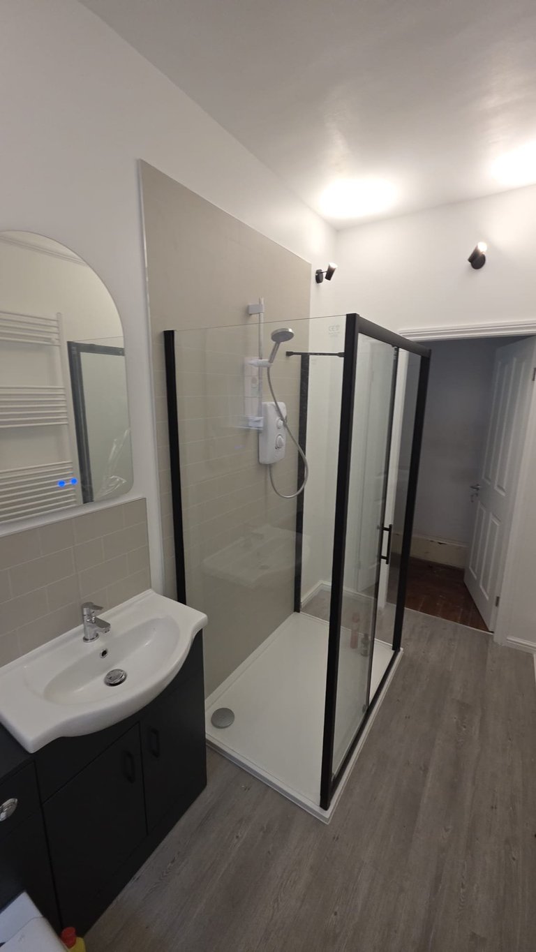 Modern bathroom with white sink, black vanity, glass shower enclosure with black frame, and white tiled walls