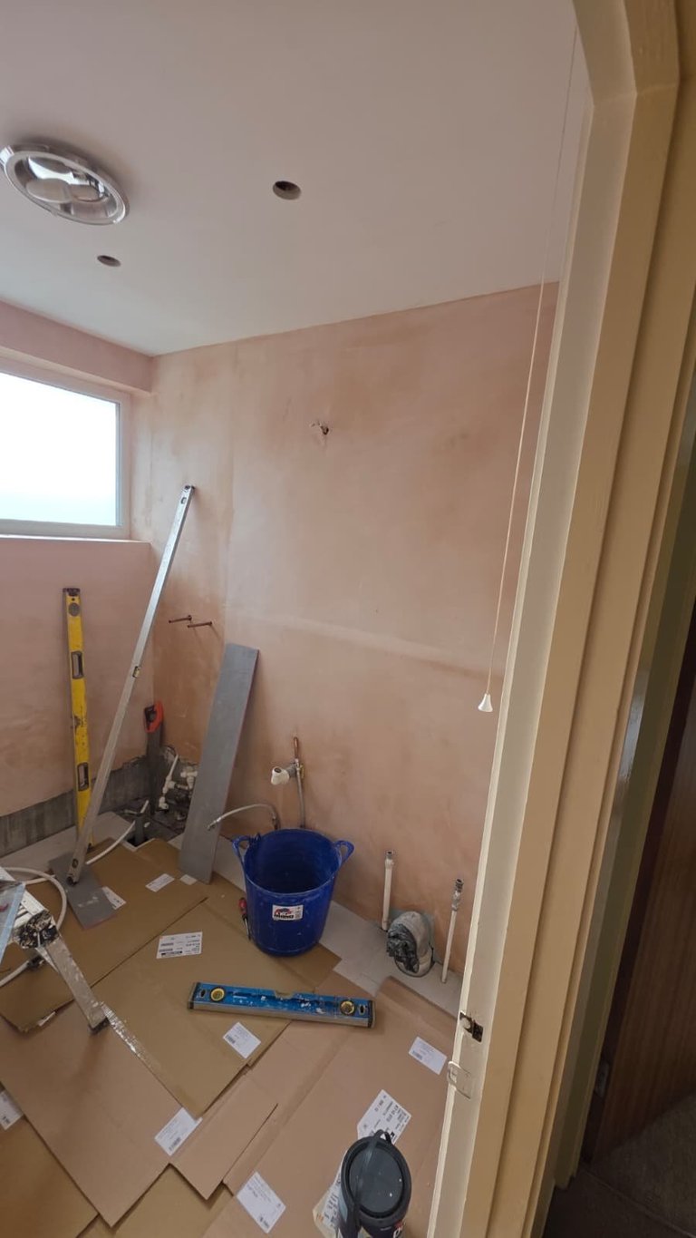 Bathroom under renovation with drywall sheets, blue bucket, level, and tools on cardboard floor protection