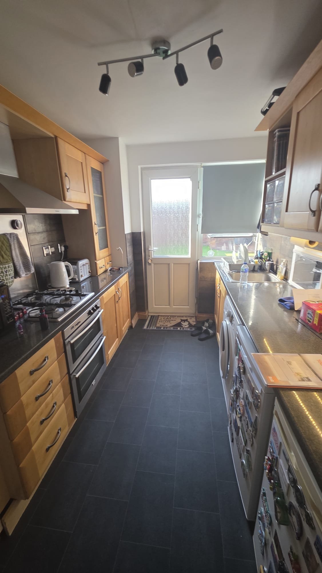 Modern galley kitchen with wooden cabinets, stainless steel appliances, black tile floor, and multiple ceiling spotlights