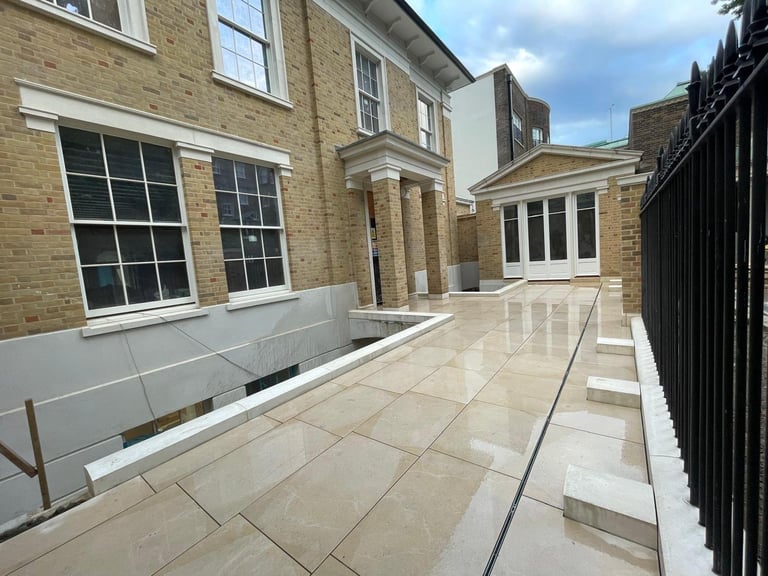 Modern patio terrace with light stone tiles surrounded by brick buildings and black railings