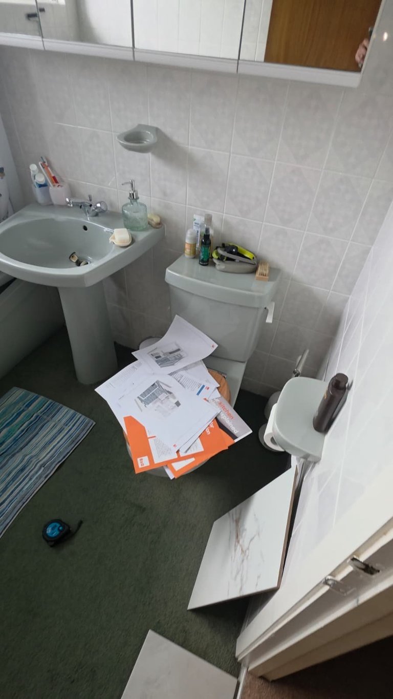 Small bathroom with cluttered floor including scattered papers, sink with toiletries, toilet, and white subway tile walls