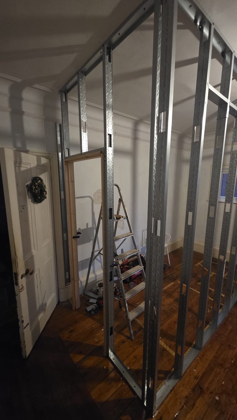 Metal stud framing for a shower enclosure under construction, with wooden floor and door frame visible in background.