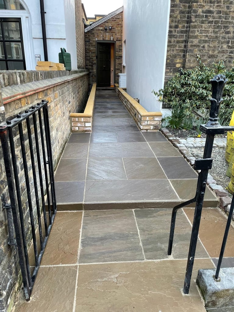 Narrow paved courtyard with slate flooring, brick walls, metal railings, and climbing ivy on the right side