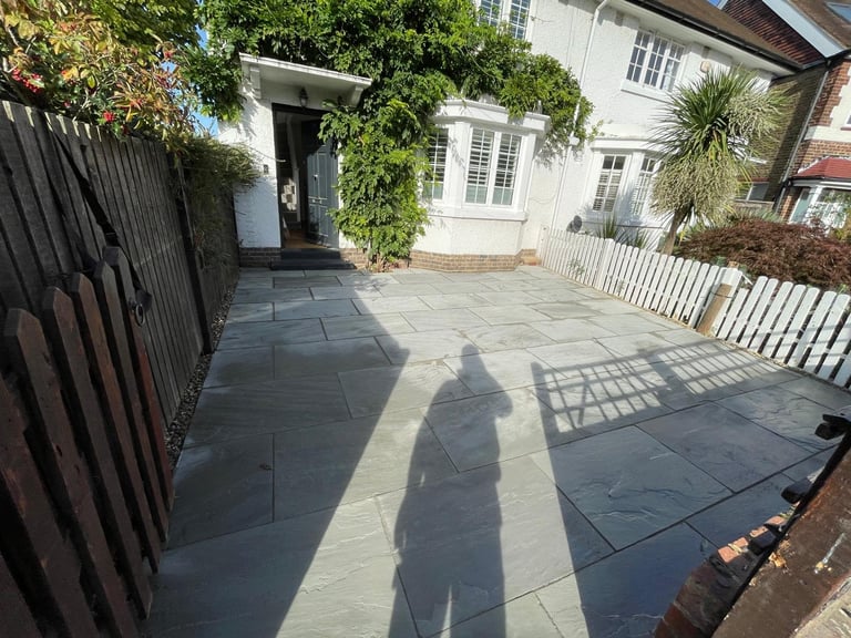 Sunny patio with dark slate tiles, white picket fence, ivy-covered entrance, and house shadow cast on ground