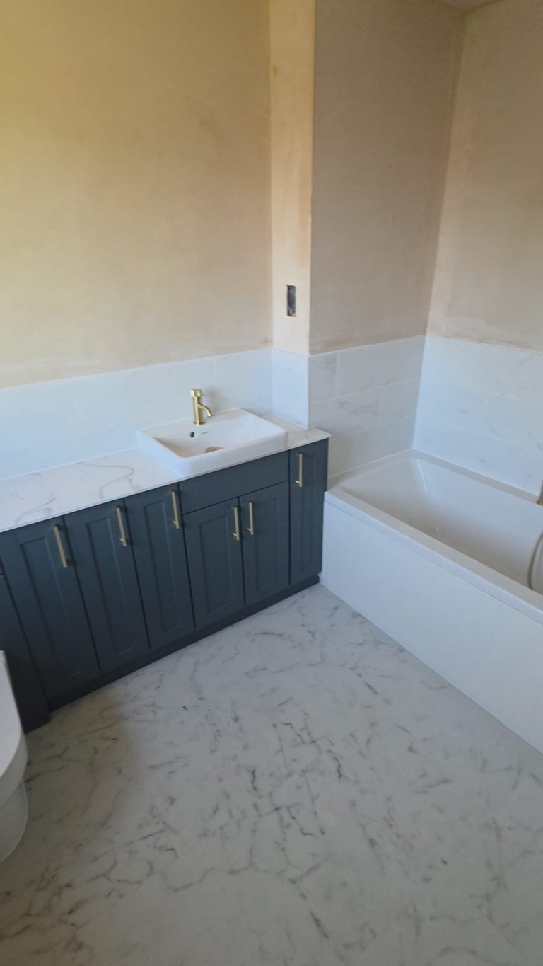 Modern bathroom with dark cabinetry, white sink, and marble-look flooring under construction